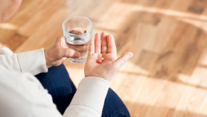 Senior adult sitting with glass of water in one hand and  holding medication in other hand