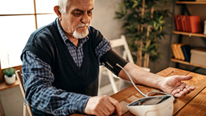 Senior adult male sitting at table taking blood pressure with a blood pressure machine