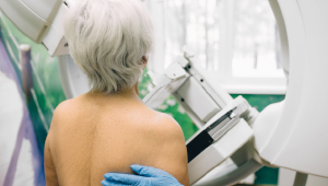 An older woman stands in front of a mammography machine, preparing for her scan